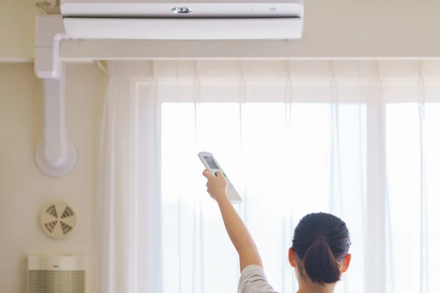 クーラーのリモコンを操作する女性